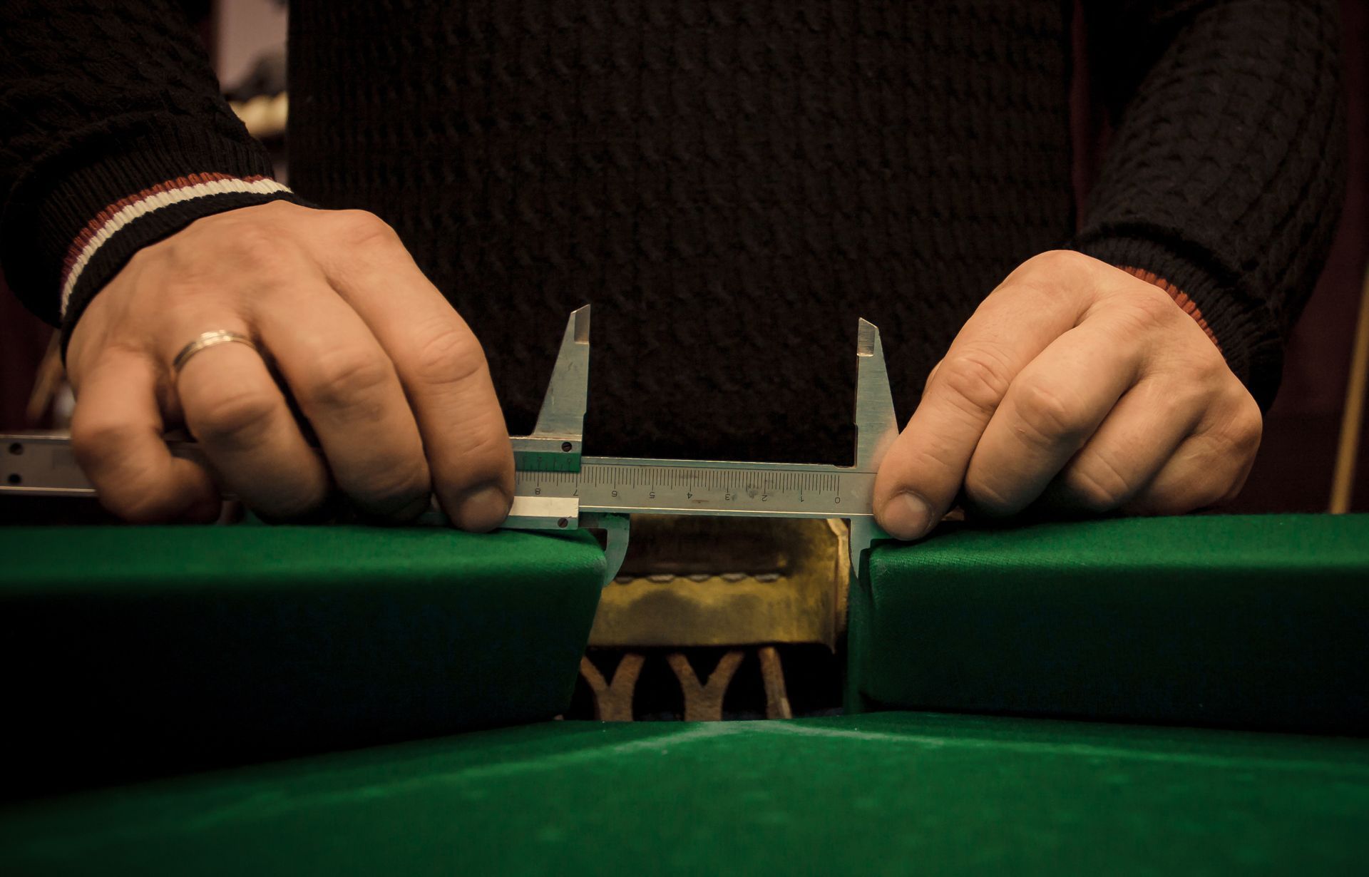 A close-up of a person measuring the length of a green pool table during a repair process A close-up of a person measuring the length of a green pool table during a repair process
