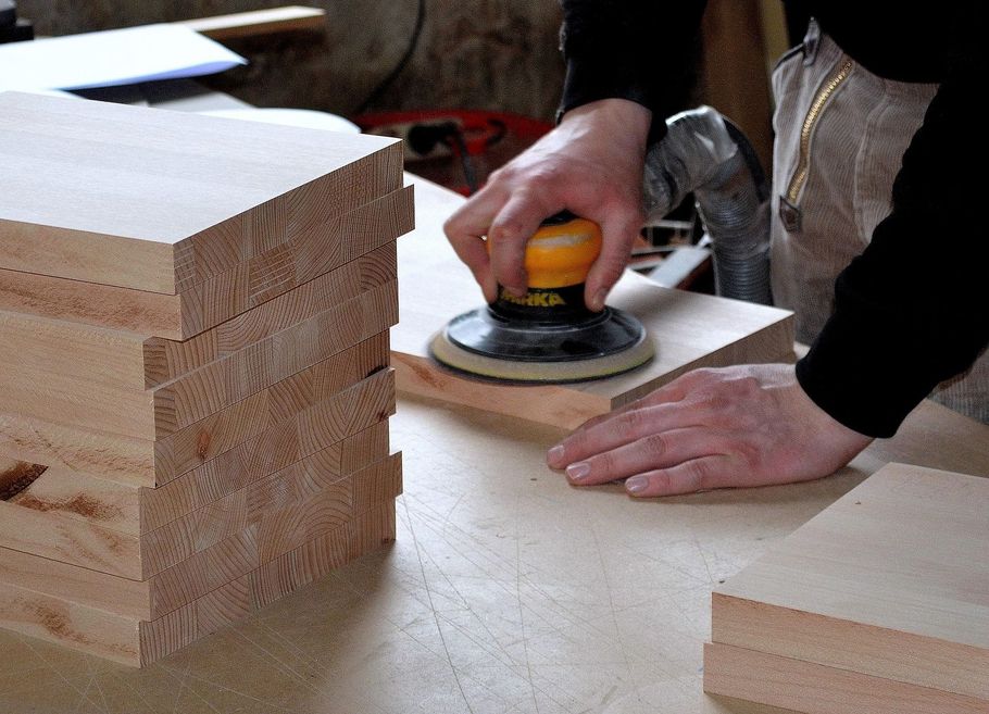 Person sanding a wooden surface with a power sander in a workshop