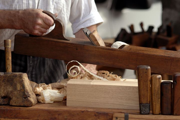 Woodworker planing a pale wooden board with shavings on a workbench