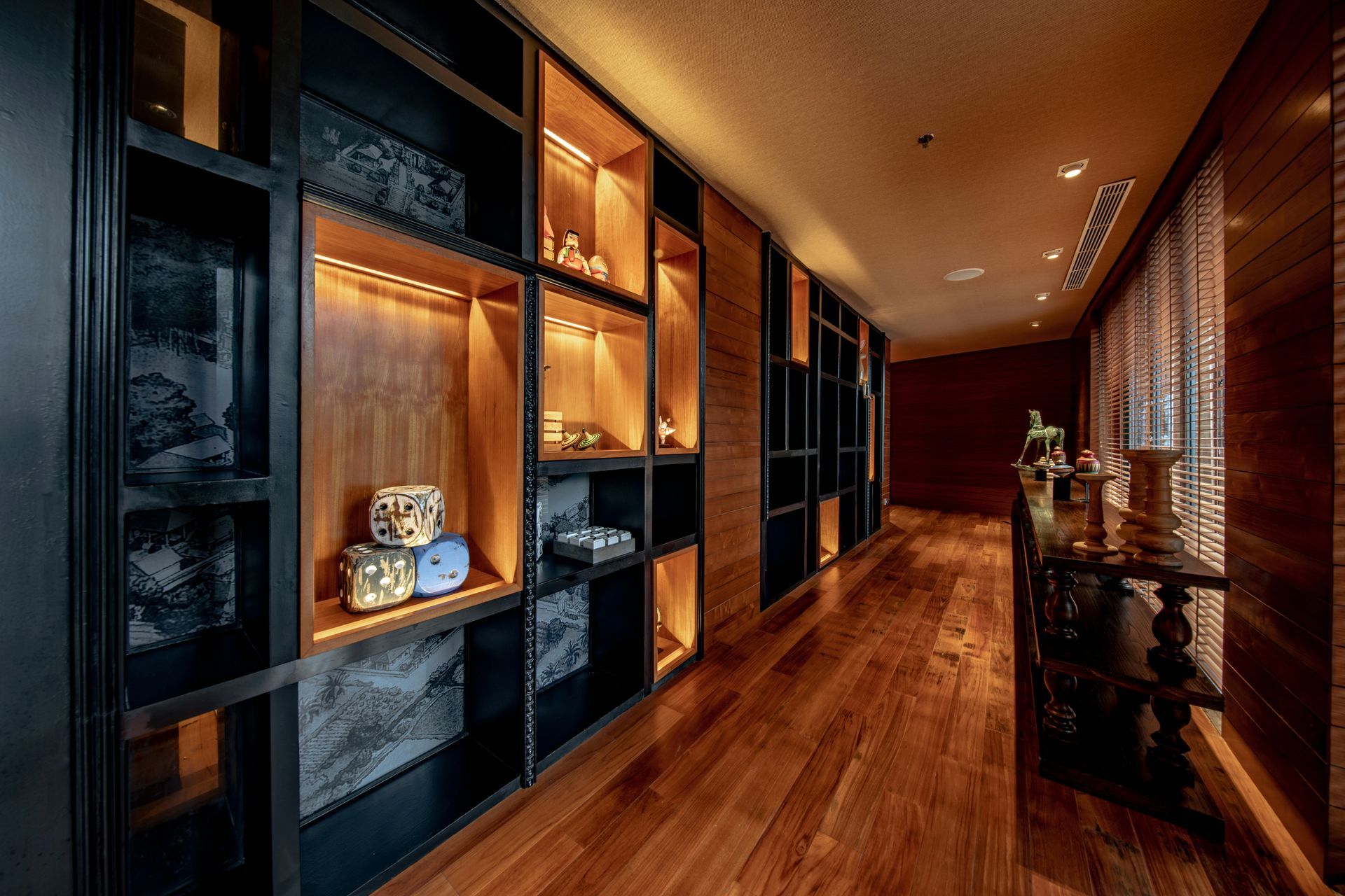 Modern hallway with warm wood flooring, black shelving, recessed lighting, and a windowed wall on the right
