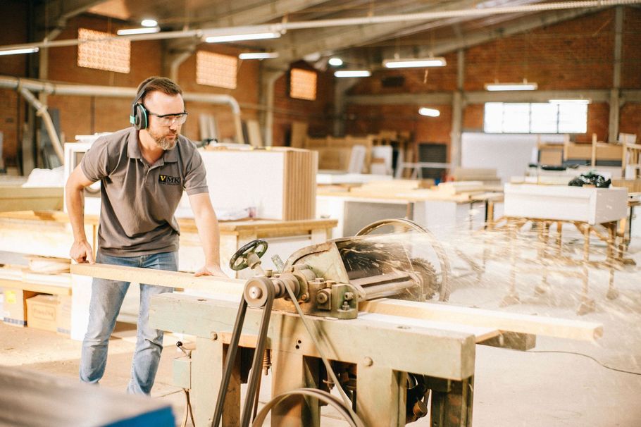 Man operating a table saw in a bright woodworking shop with lumber and tools nearby
