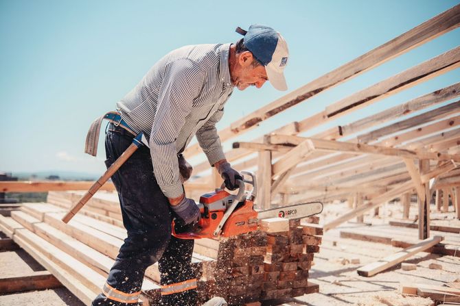 Construction worker cutting lumber on a roof with a circular saw, surrounded by wooden framing.