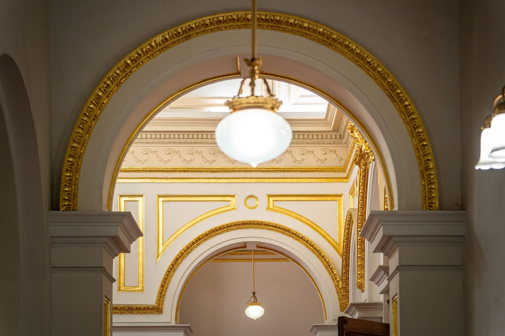 Ornate white and gold arched hallway with hanging globe lights in a grand interior