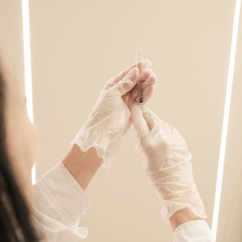Gloved hands holding a small test tube against a plain beige background
