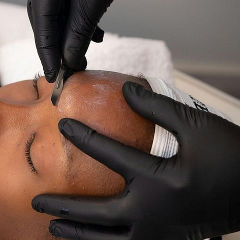Gloved hands applying a facial treatment to a person’s forehead in a spa setting