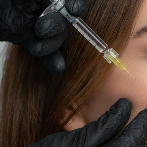 Gloved hands apply a clear serum with a dropper to a person’s cheek