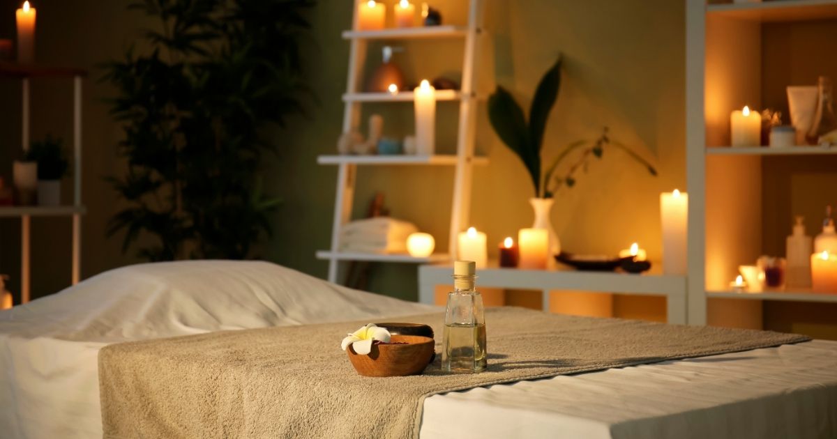 Cozy spa room with a massage table, candles, shelves, plants, and warm ambient lighting