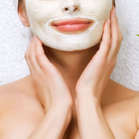 Woman with white facial mask gently touching her face in a spa setting