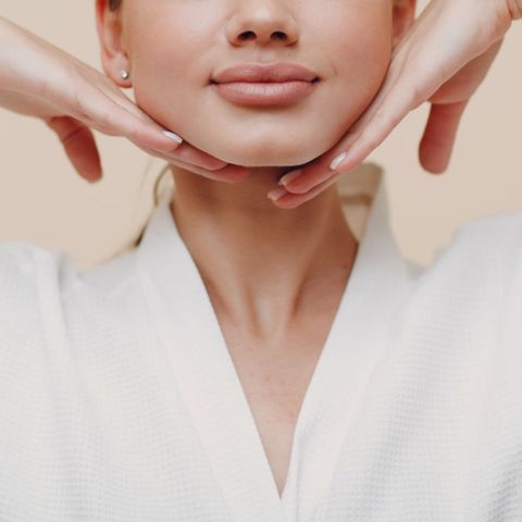 Close-up of a person in a white robe resting their chin on both hands, with a soft neutral background