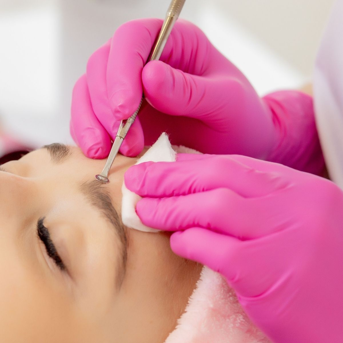 Gloved hands shaping eyebrows with tweezers on a person’s face during a beauty treatment