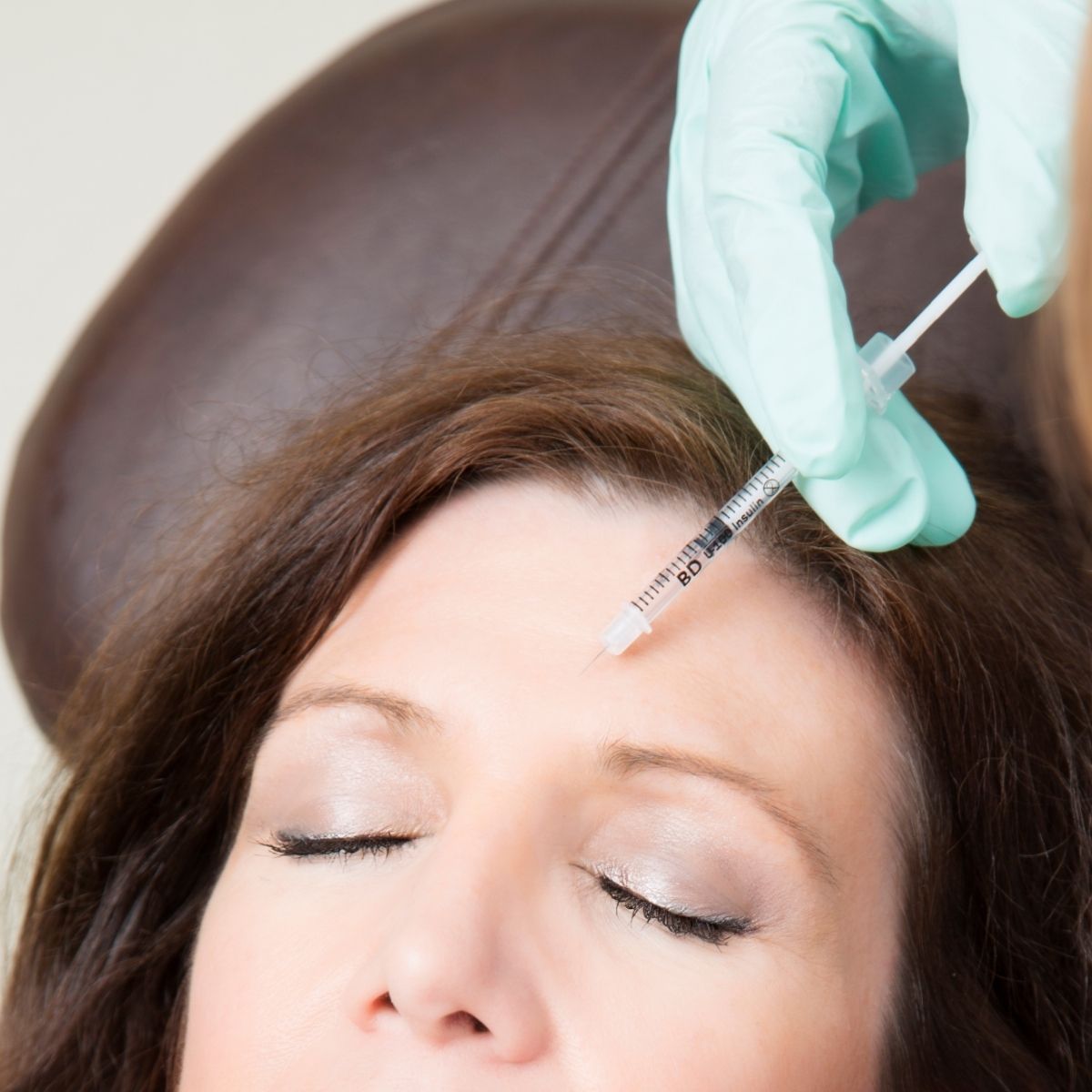 Healthcare professional injecting a syringe into a woman’s forehead during a cosmetic treatment