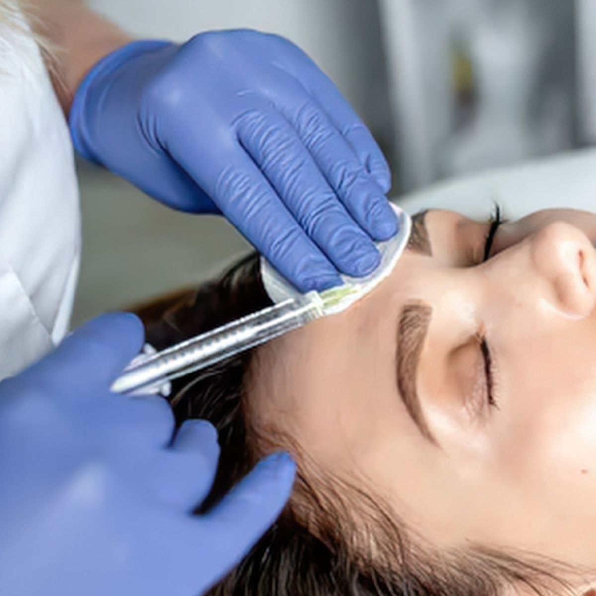 Gloved hands cleaning a patient’s eyebrow with a cotton swab during a cosmetic treatment