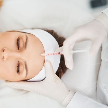 Gloved hands injecting facial filler into a woman’s forehead in a clinic setting