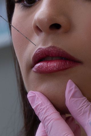 Close-up of lips and nose with a gloved hand applying beauty treatment