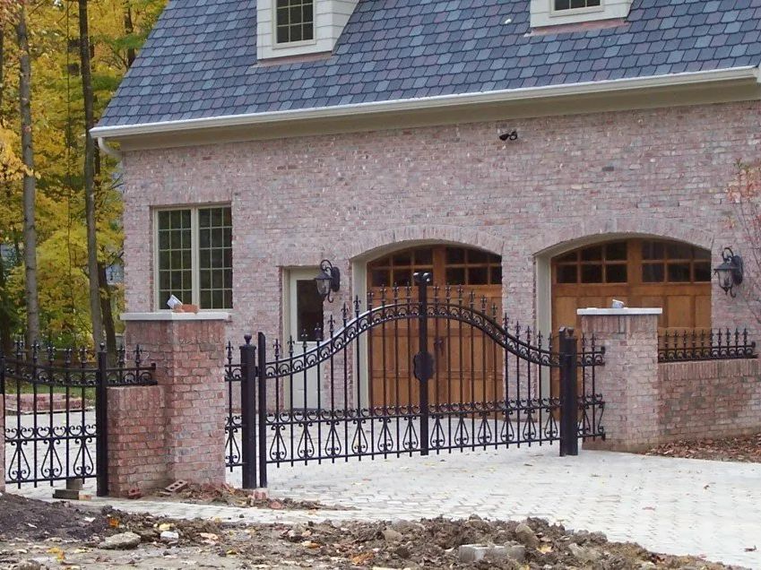 Black wrought-iron gate in front of a brick building with a driveway and garage doors.