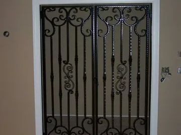 Black wrought iron security doors in a doorway with tan walls and white trim.