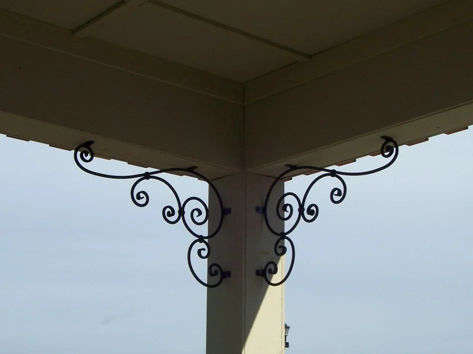 Ornate black metal decorative brackets attached to a beige wooden porch corner.