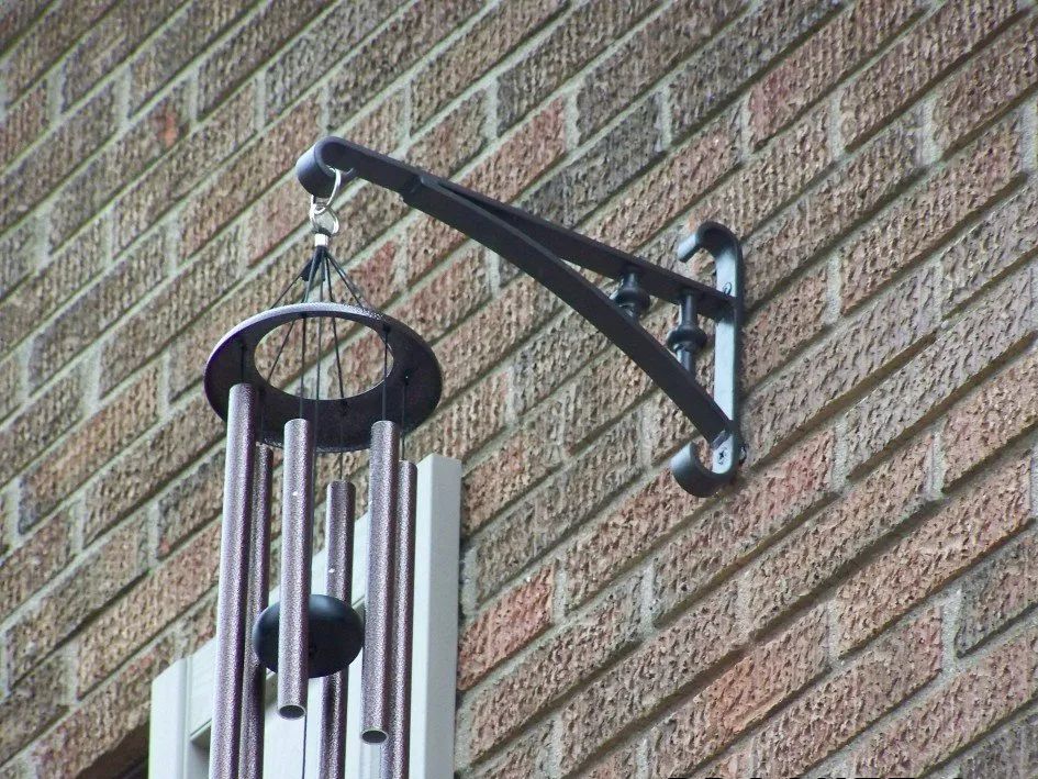 Black metal bracket holding a wind chime against a brick wall.