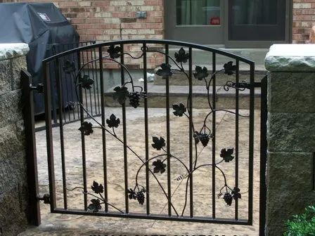 Black wrought-iron gate decorated with grapevines, set in a stone wall opening.