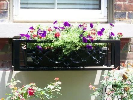Black window box overflowing with purple and red flowers against a brick wall.