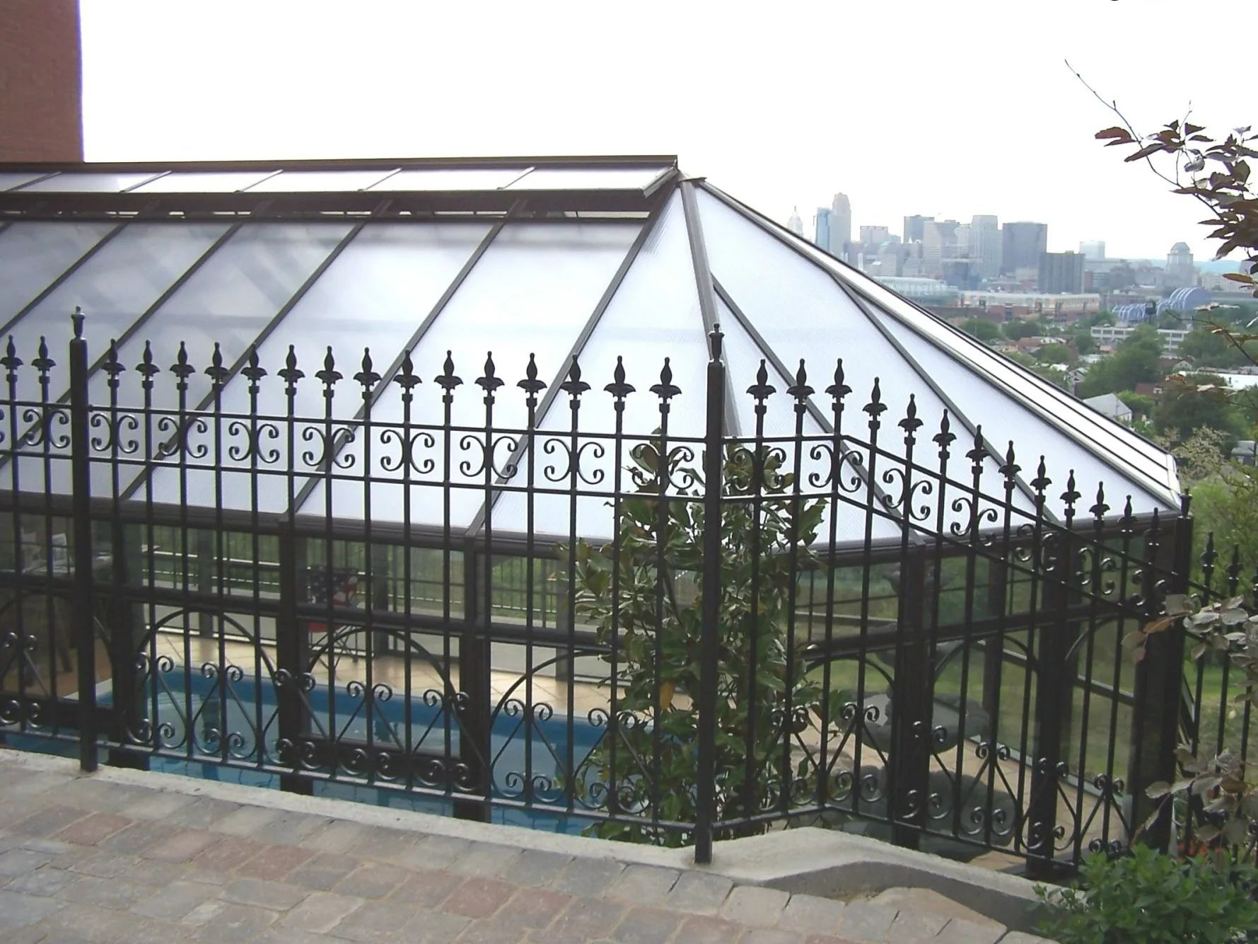 Greenhouse with a black wrought iron fence overlooking a city skyline.