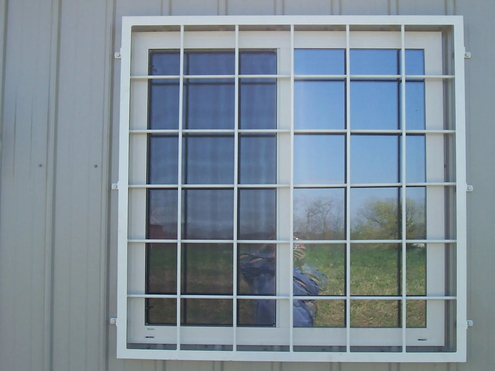White-framed window with a grid security grille on a light gray building.
