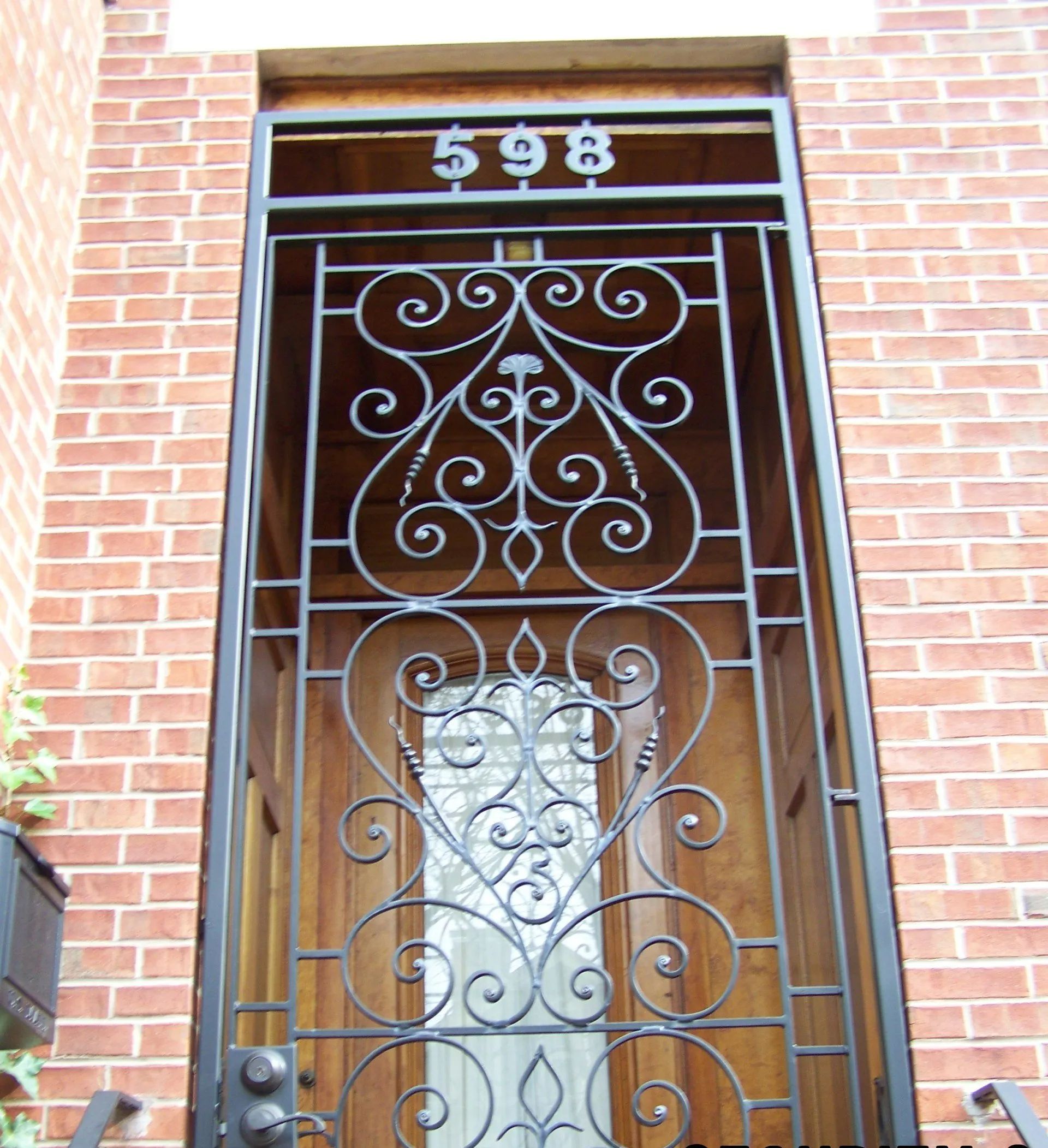 Ornate iron security gate over wooden door with house number 598 on brick building.