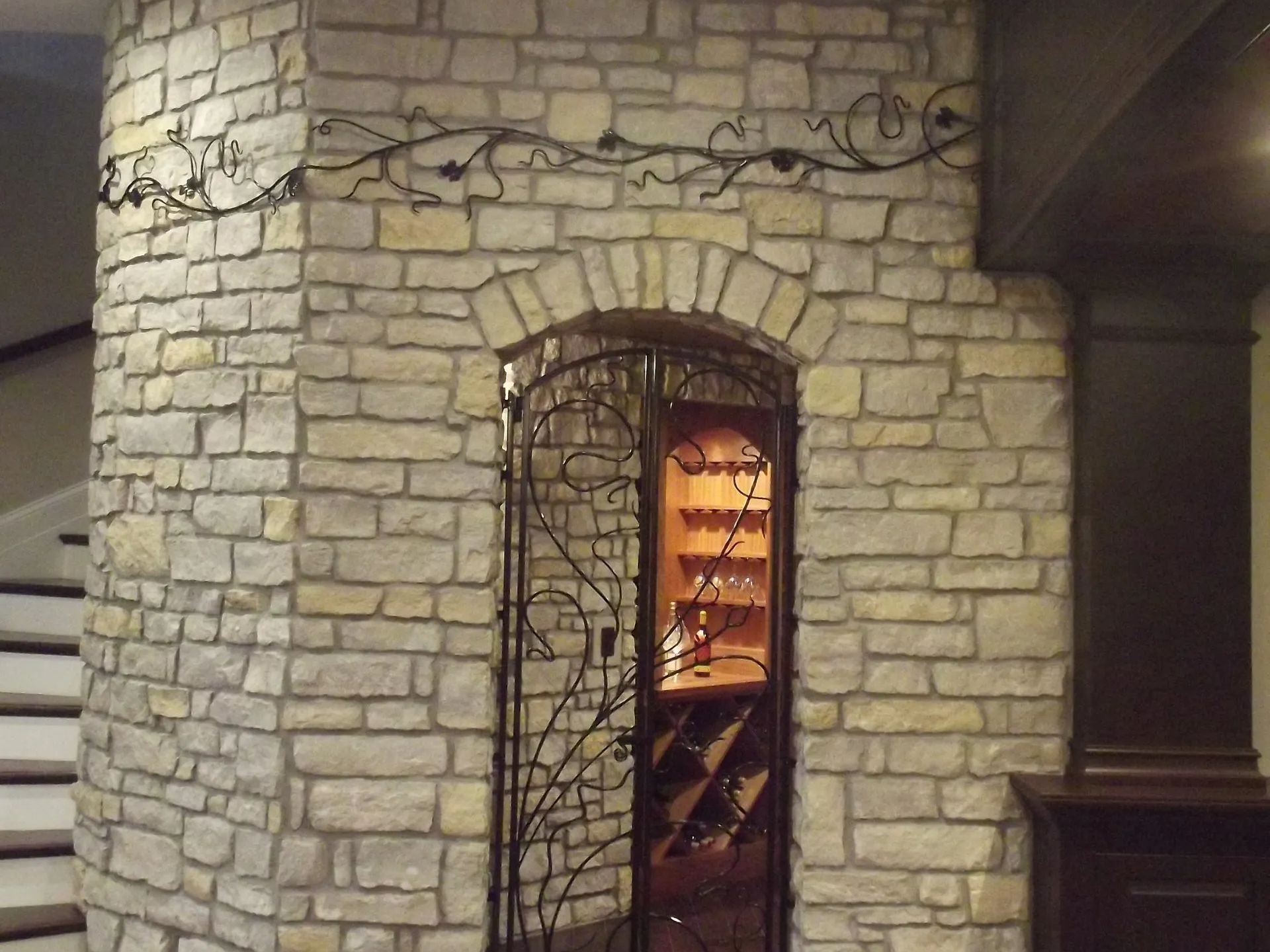 Stone wall with arched doorway, decorative metal gate, and wine storage.