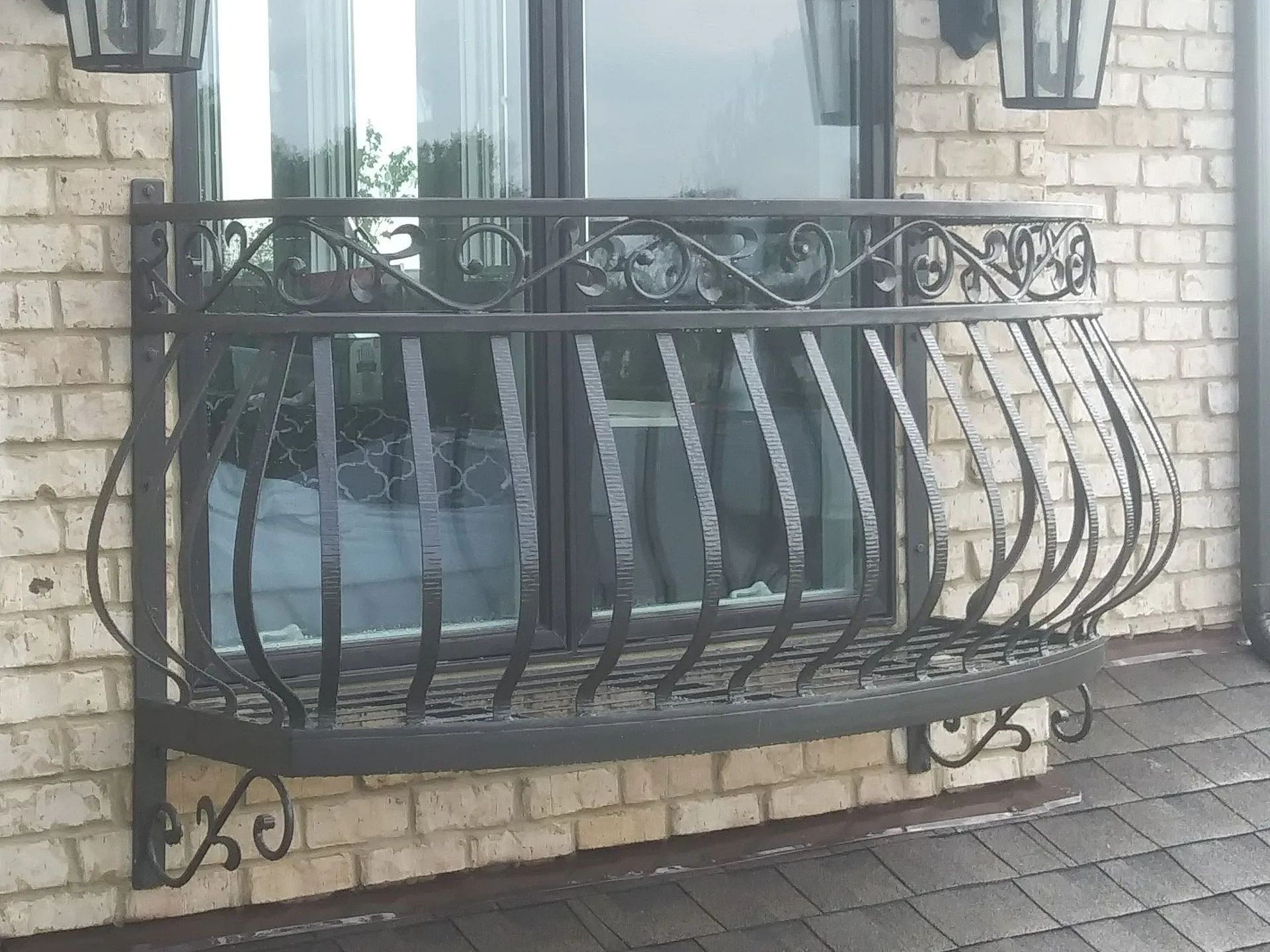 Black wrought iron window box on brick wall with curved bars and decorative scrollwork.