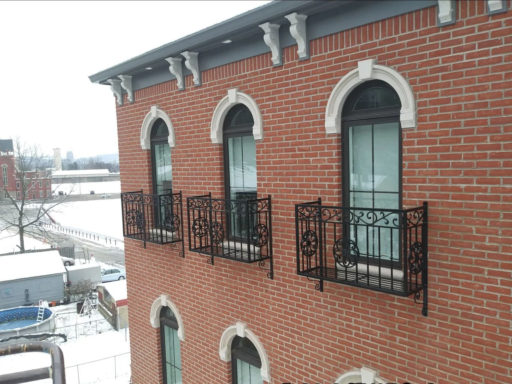 Red brick building with arched windows, decorative iron railings, and snow-covered surroundings.
