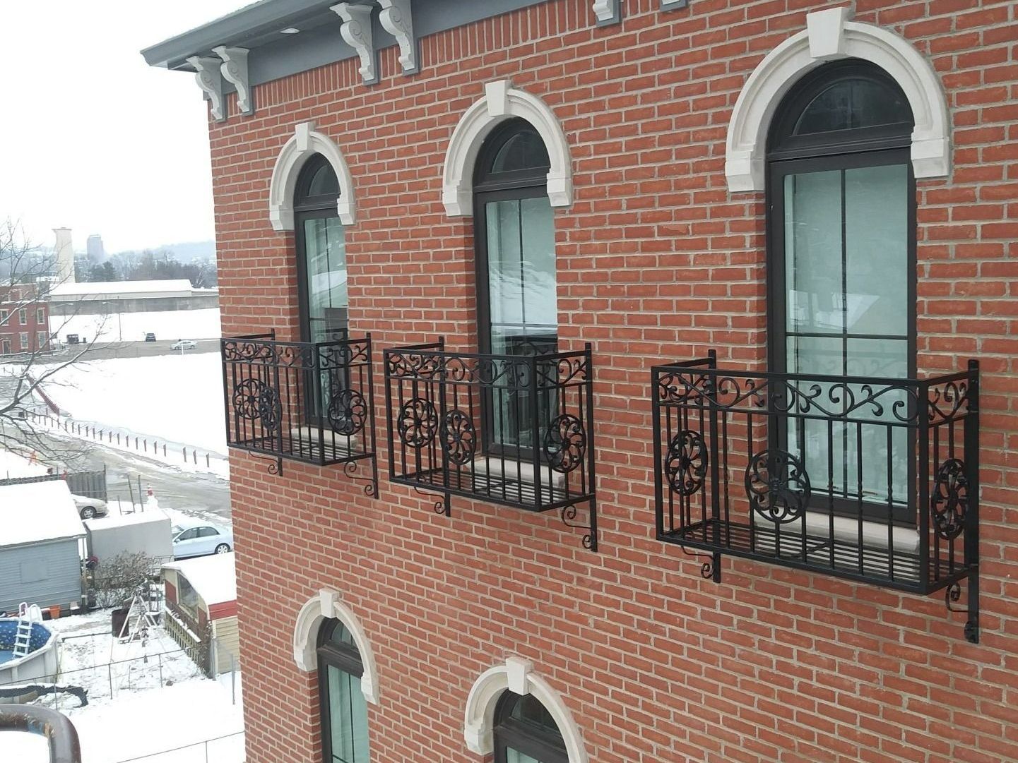 Red brick building with arched windows, wrought iron balconies, and snow-covered surroundings.