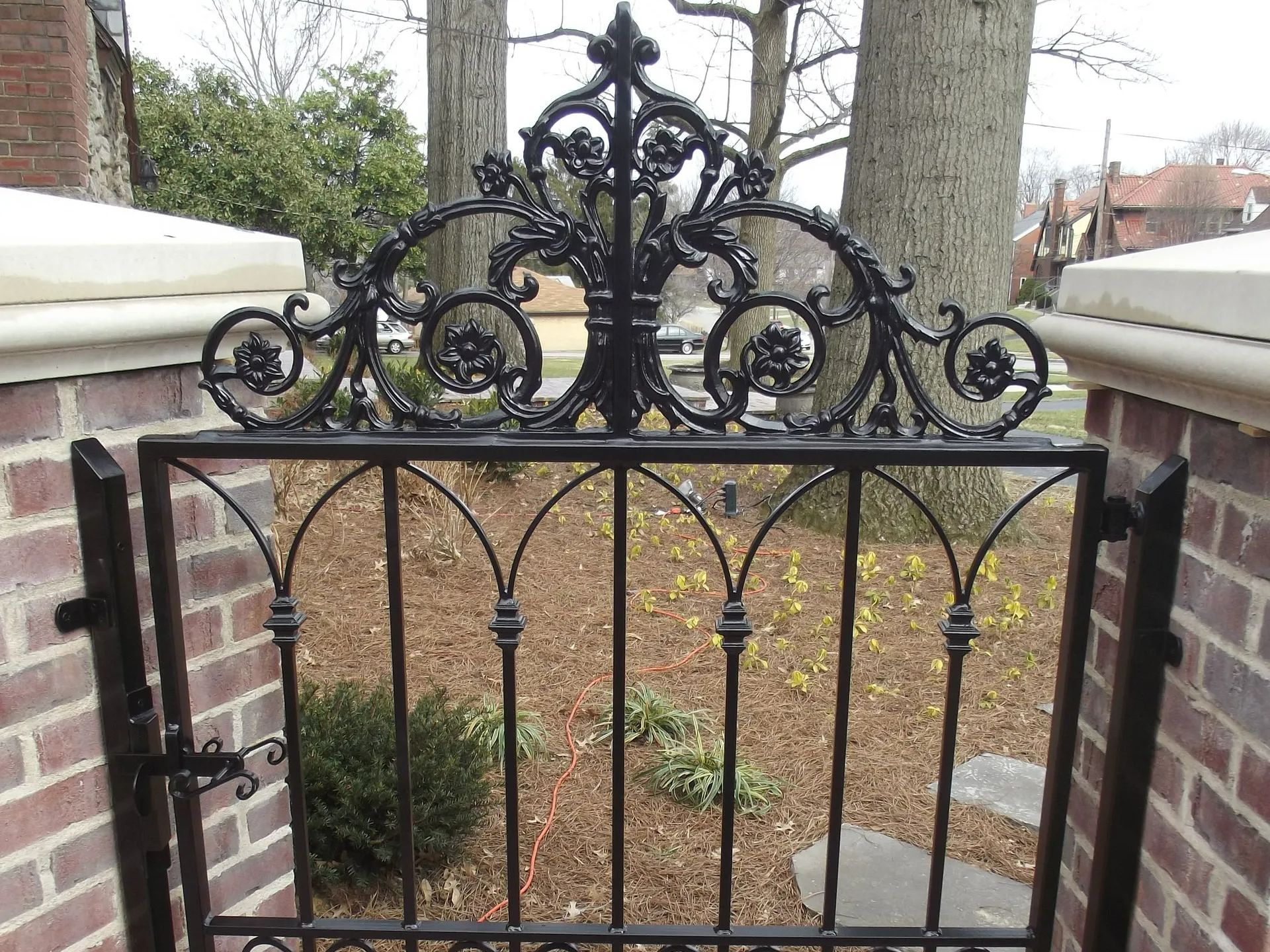 Black iron gate with ornate scrollwork, set in a brick and stone entryway.