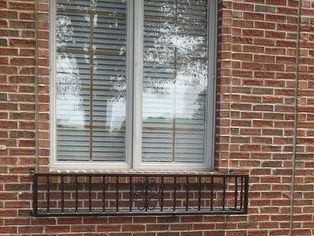 Window with gray blinds and a black metal window box on a red brick wall.