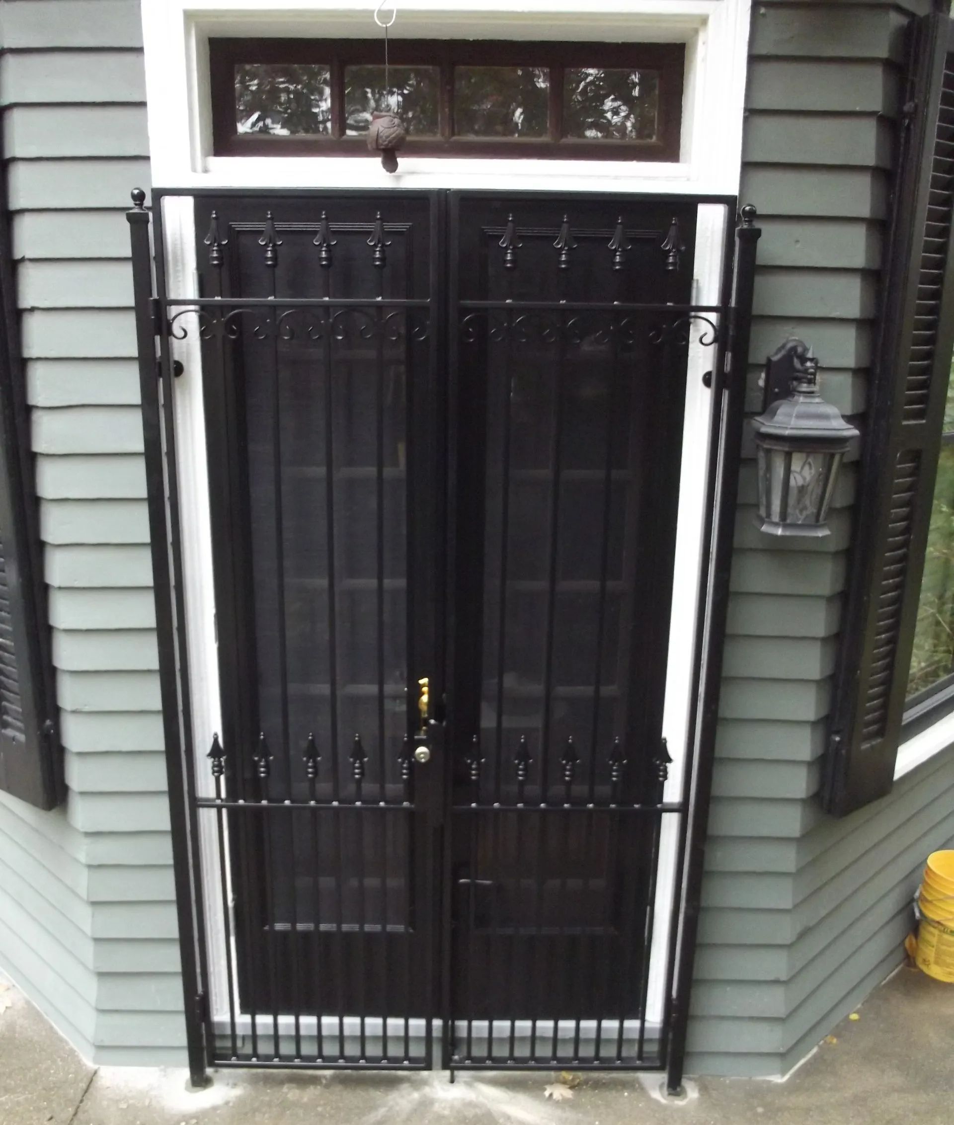 Black double doors with ornate iron gate in a gray house doorway.