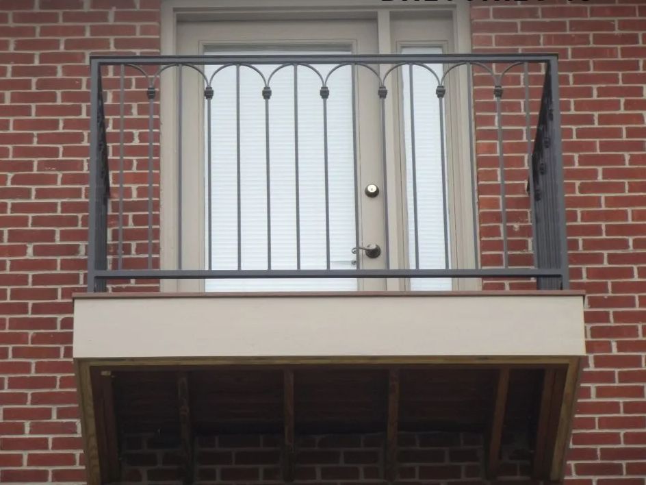Small balcony with metal railing, attached to red brick building, french doors.