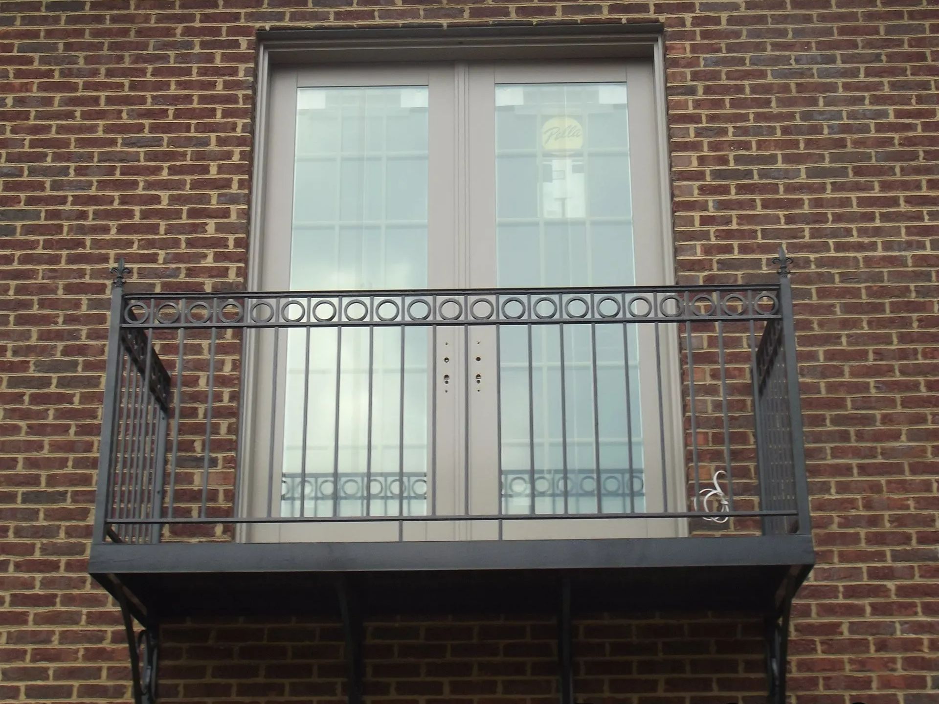 Brick building with light-colored double doors leading to a small iron balcony with a decorative railing.