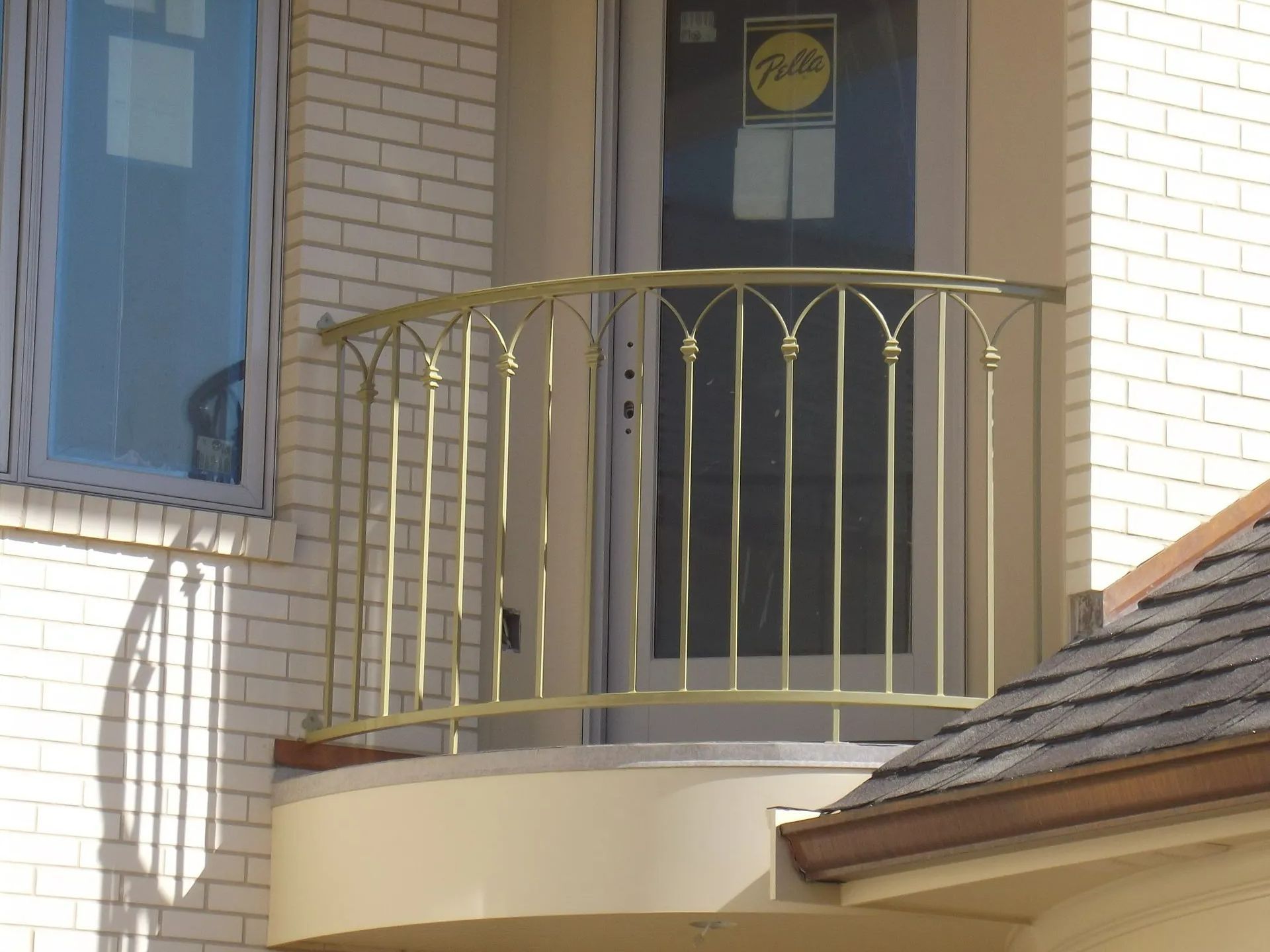 Golden metal balcony railing in front of a glass door on a brick building.