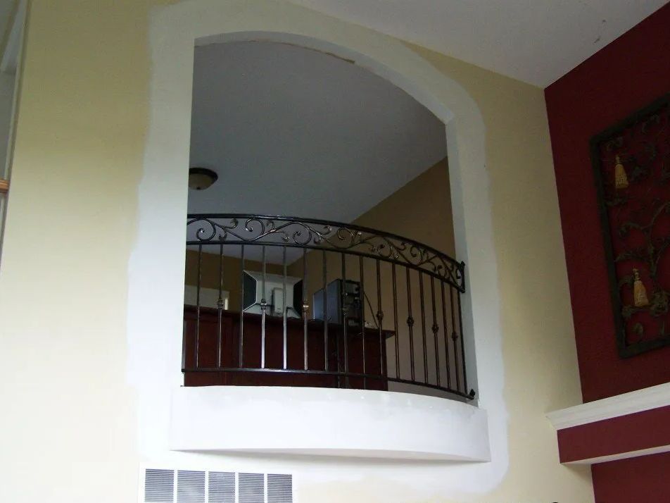 Interior view of arched doorway with railing, looking into a room with a desk and computer.