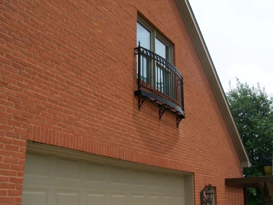 Brick building with a garage door and window with black wrought-iron balcony.