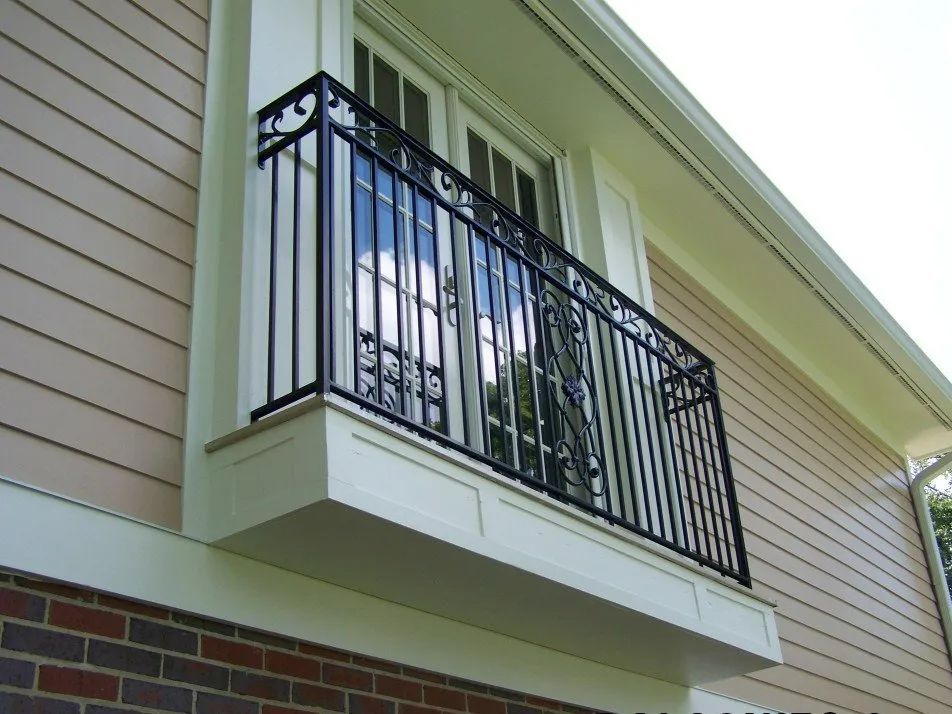 Black wrought-iron balcony railing outside a window on a tan house with white trim.