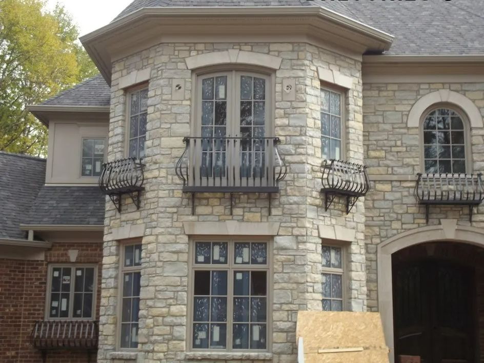 Stone house facade with arched windows, wrought-iron balconies, and neutral-toned trim.