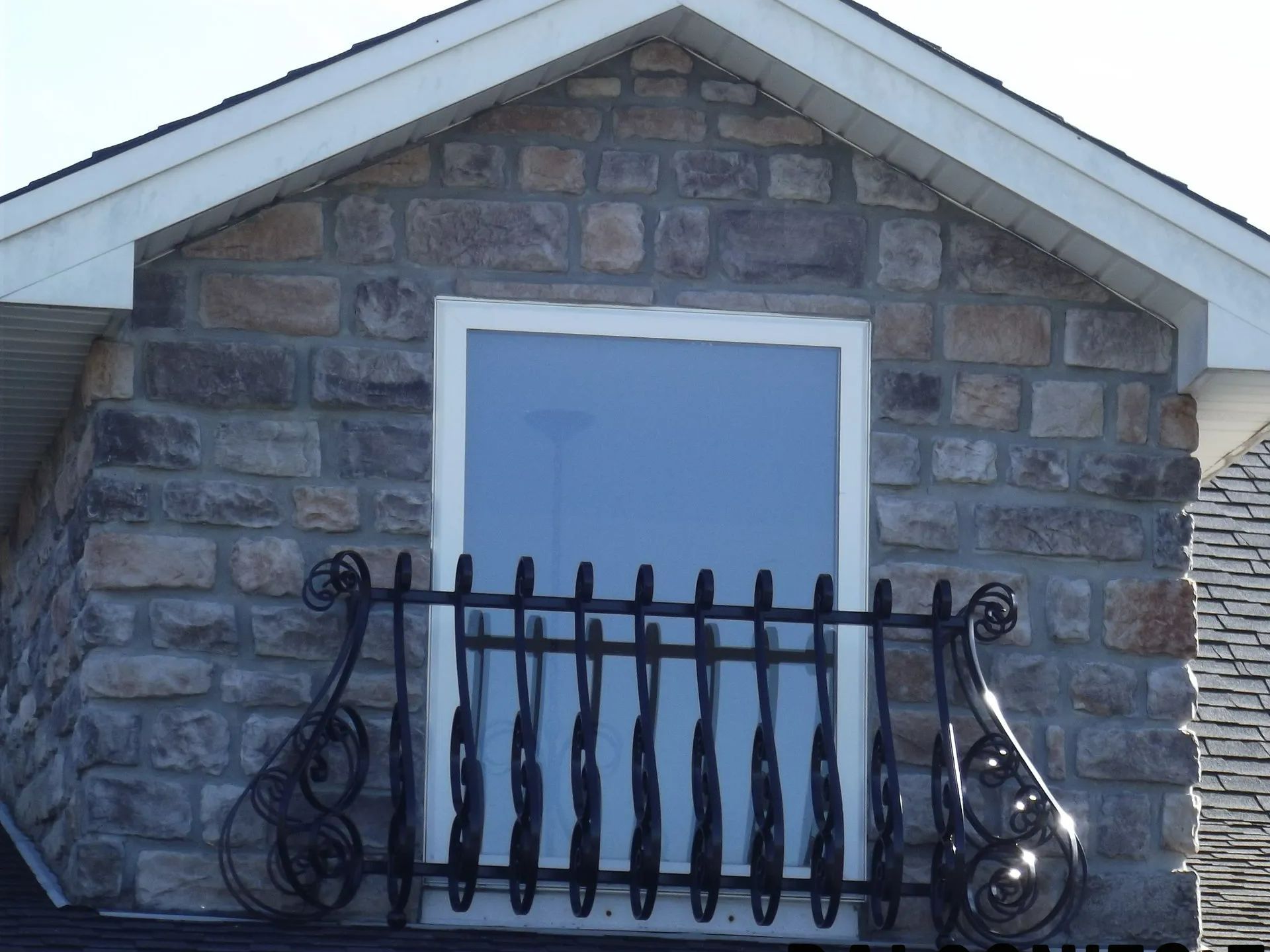 Stone building facade with a window and black metal railing.