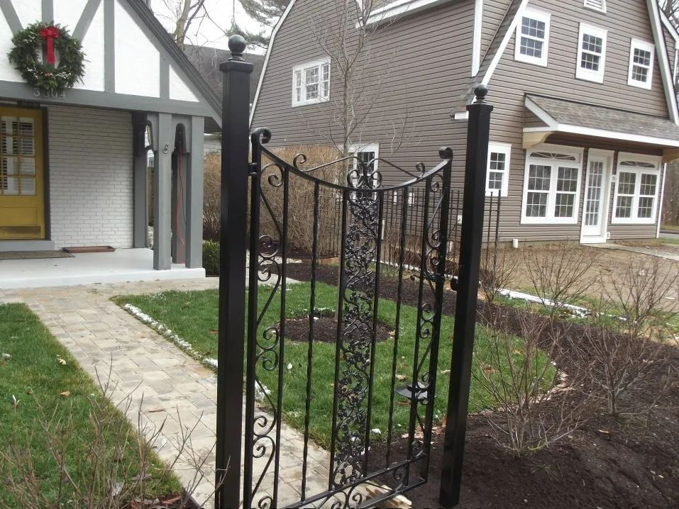 Black iron gate in front of a house. Paved walkway leads to the front door with a wreath.