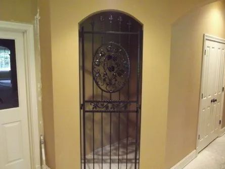 Iron gate in a recessed arched doorway, between tan walls and two white doors.