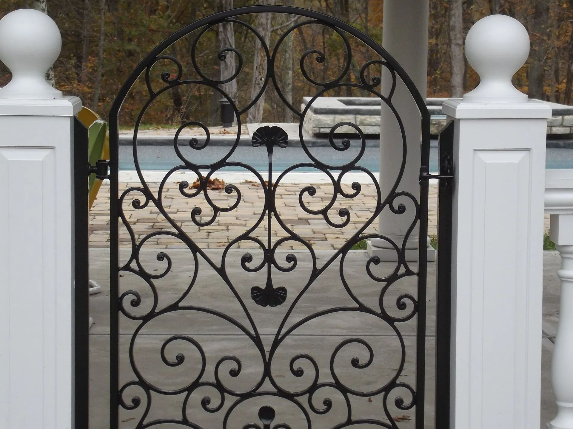 Black wrought iron garden gate with decorative scrollwork between white pillars.