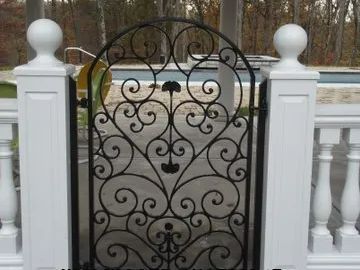 Black wrought iron gate in white fence leading to a pool.