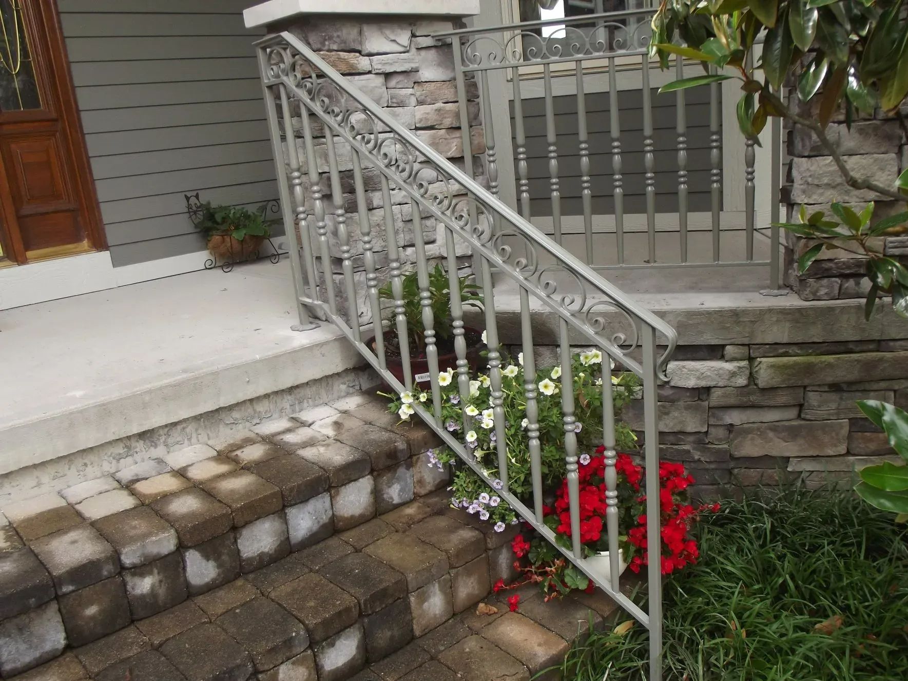 Gray metal handrail on brick steps with flowers.
