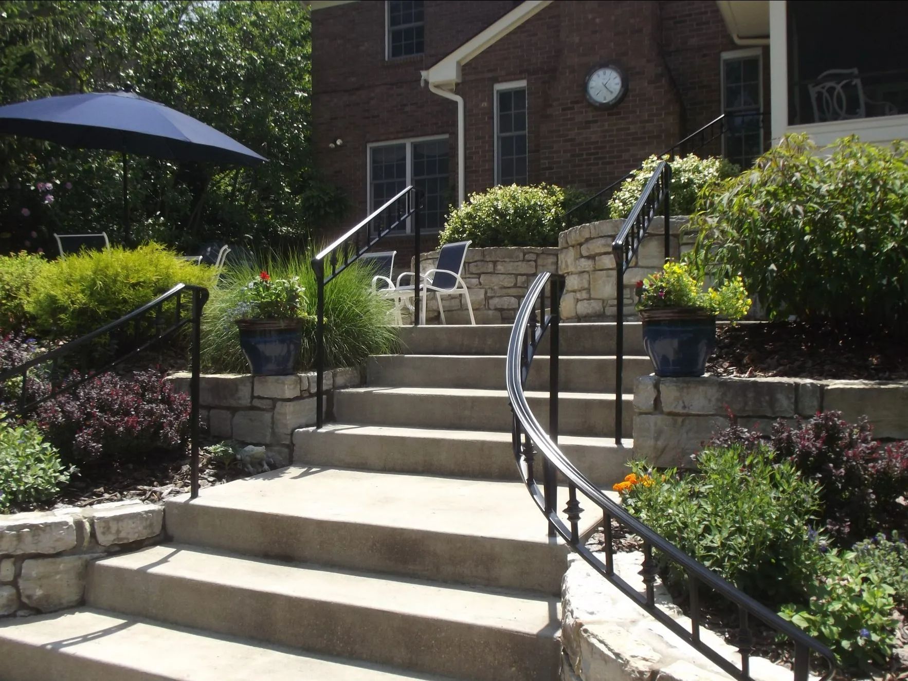 Stone steps lead to a brick house, with black railings and surrounding landscaping.