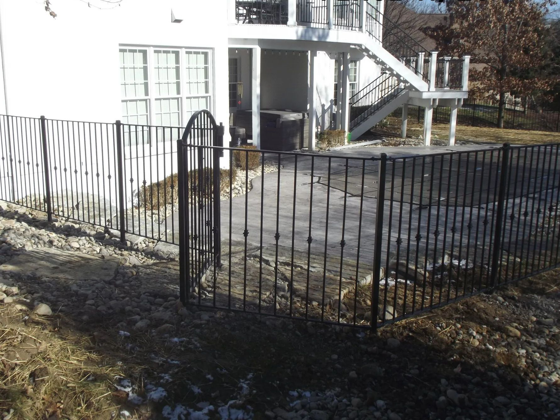 Black metal fence encloses a concrete patio near a white house with a deck.