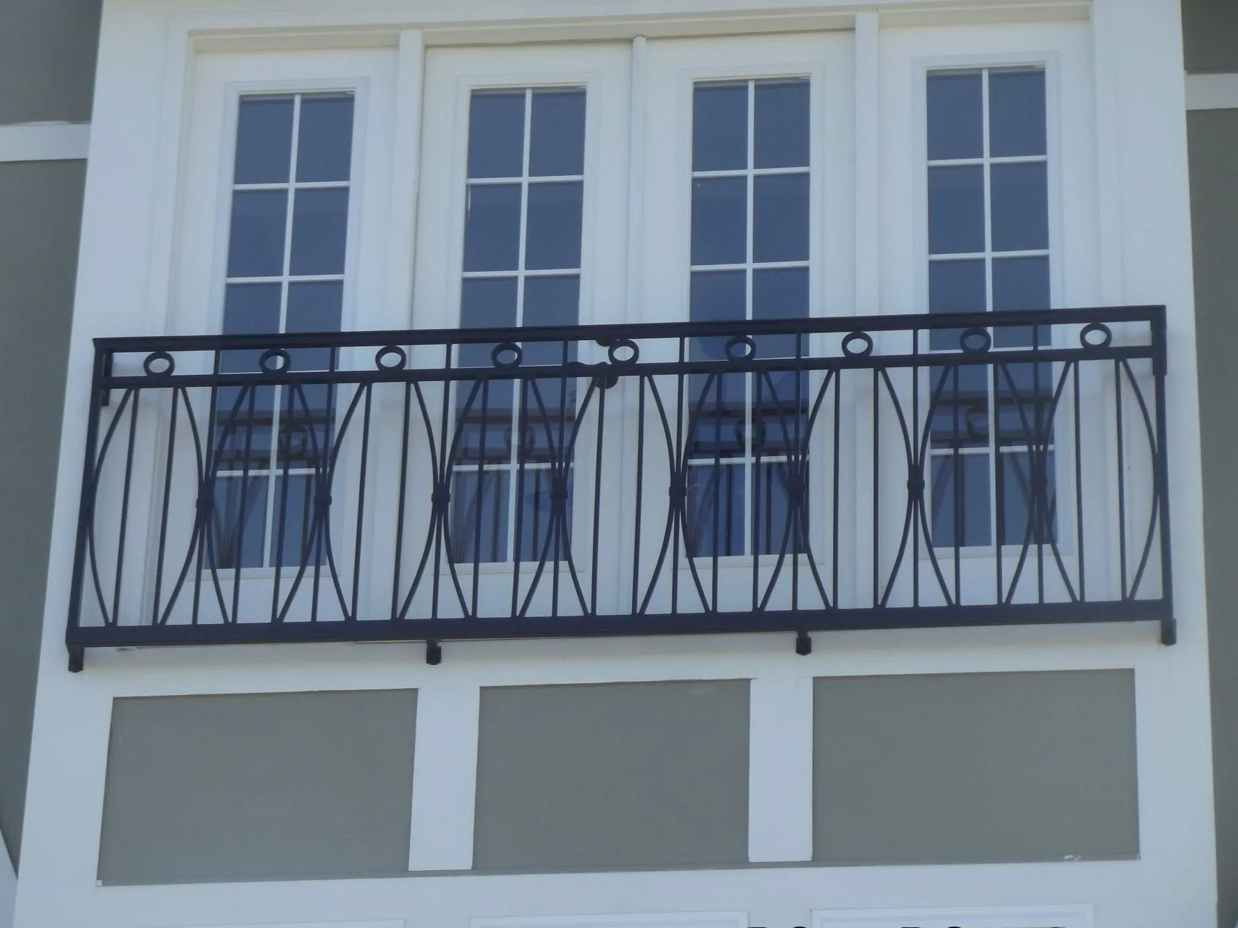 Black wrought iron balcony railing in front of white-framed windows on a gray building.